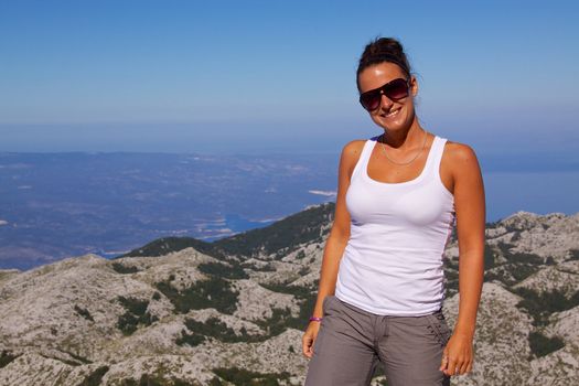 Smiling young girl on hilltop with beautiful panorama of nature park Biokovo on Dalmatian coast near Makarska Riviera in Croatia in the background