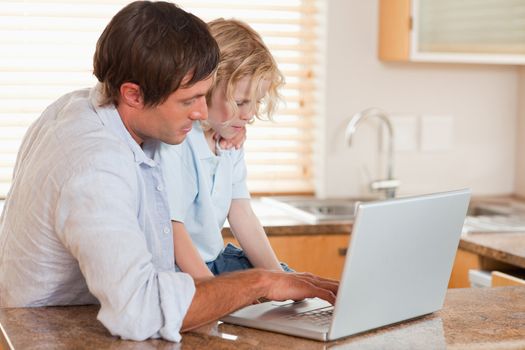 Boy and his father using a laptop together in a kitchen