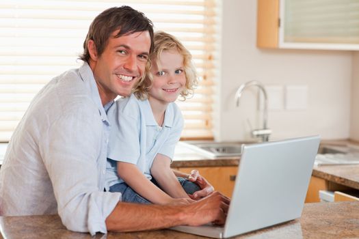 Boy and his father using a notebook together in a kitchen