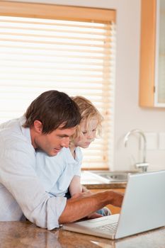 Portrait of a boy and his father using a laptop together in a kitchen