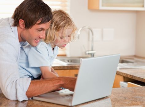 Cute boy and his father using a laptop together in a kitchen