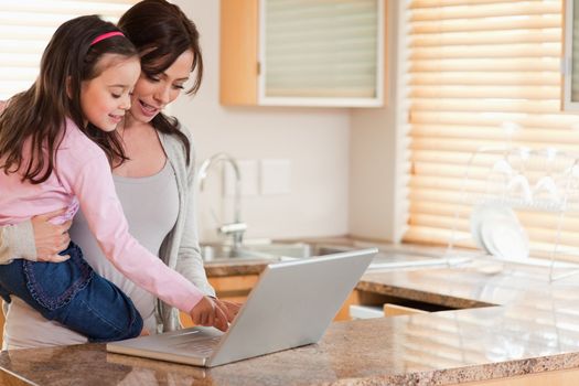 Girl and her mother using a laptop in a kitchen