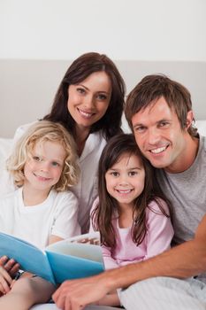 Portrait of a happy family reading a book in a bedroom