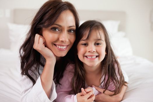 Mother and her daughter lying on a bed while looking at the camera