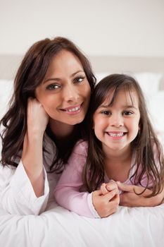 Portrait of a mother and her daughter lying on a bed while looking at the camera