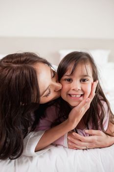 Portrait of a mother kissing her daughter in a bedroom