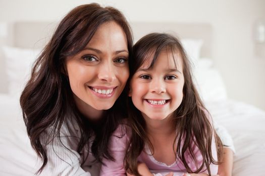 Girl and her mother lying on a bed while looking at the camera