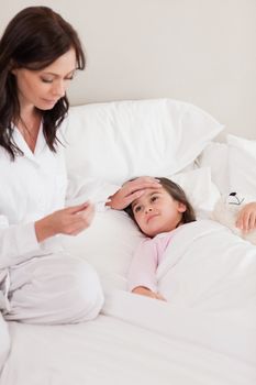 Portrait of a mother checking on her daughter's temperature in a bedroom