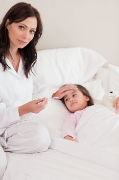 Portrait of a concerned mother checking on her daughter's temperature in a bedroom