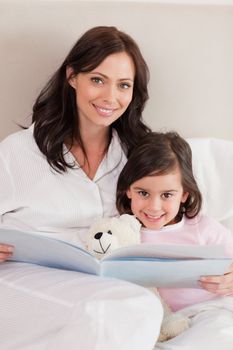 Portrait of a happy mother reading a story to her daughter in a bedroom