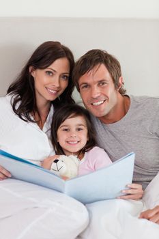 Portrait of parents reading a story to their daughter in a bedroom
