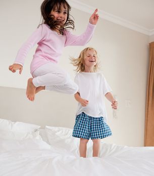 Portrait of playful siblings jumping on a bed