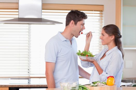 Happy couple tasting a salad in their kitchen
