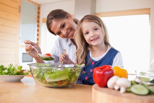 Happy mother and her daughter preparing a salad in their kitchen