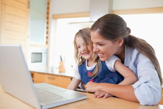 Smiling mother and her daughter using a laptop in their kitchen