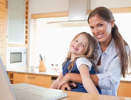 Happy mother and her daughter using a laptop in their kitchen