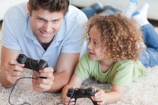 Boy and his father playing video games while lying on a carpet