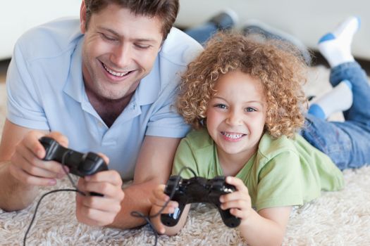 Happy boy and his father playing video games while lying on a carpet