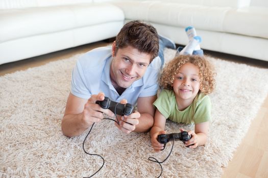 Smiling boy and his father playing video games while lying on a carpet