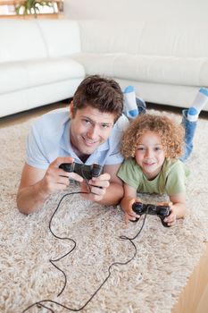 Portrait of a boy and his father playing video games while lying on a carpet