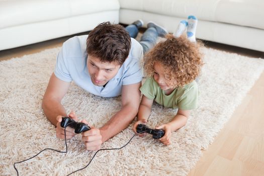 Focused boy and his father playing video games while lying on a carpet