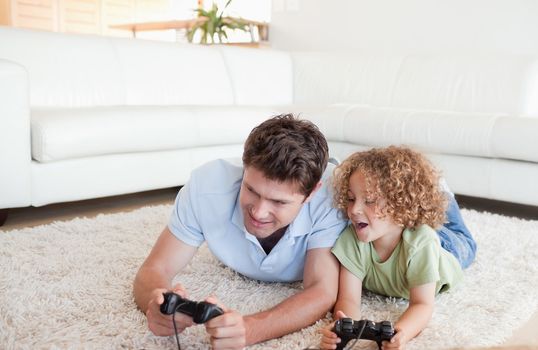 Cheerful boy and his father playing video games while lying on a carpet