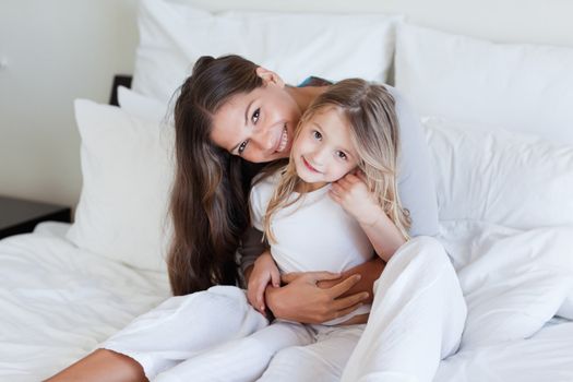 Mother and her daughter posing on a bed while looking at the camera