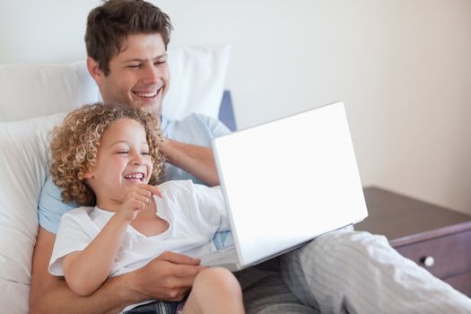Father and child using laptop together in bed