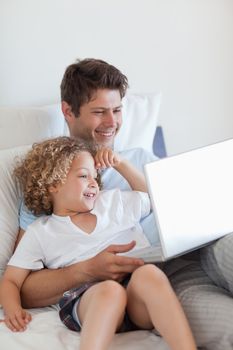 Smiling father and child on bed with laptop together