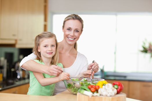 Smiling mother and daughter stirring salad together