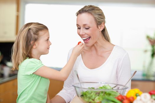 Little girl feeding her mother with tomato