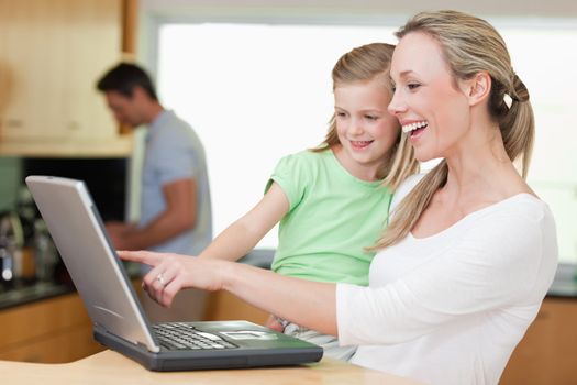 Happy mother and daughter using laptop together with father in the background