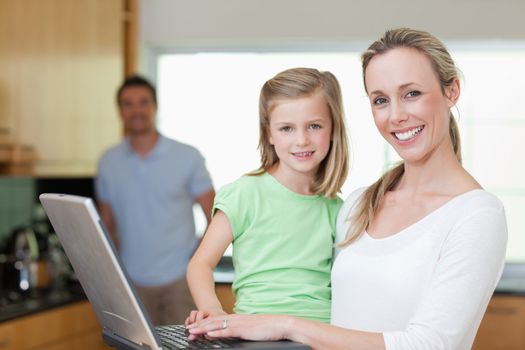 Mother and daughter using laptop together with father in the background