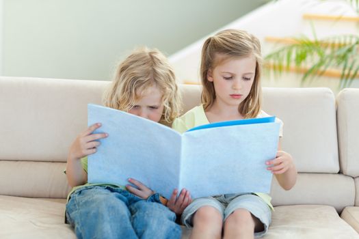 Siblings reading magazine together on the sofa