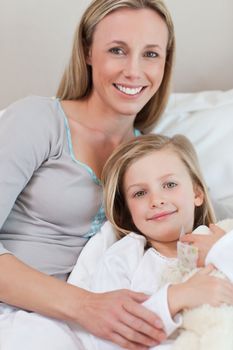 Smiling mother holding her daughter on the bed