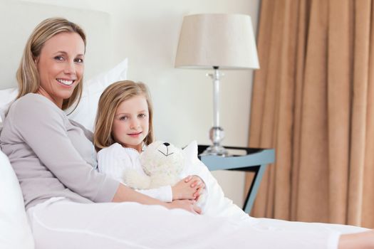 Side view of mother and daughter sitting together on the bed