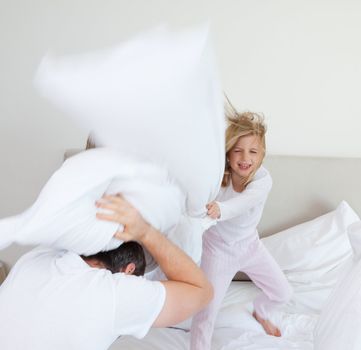 Little girl hitting her father with pillow