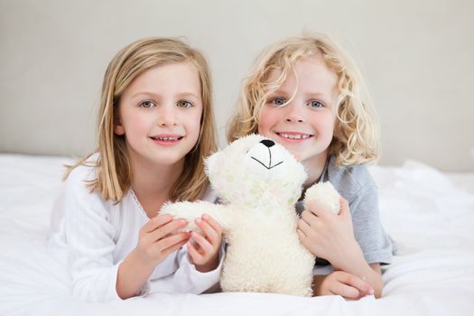 Siblings lying on the bed together with teddy