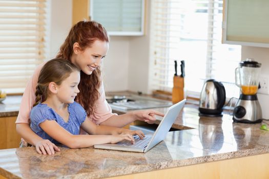 Mother and daughter together with laptop behind the kitchen counter