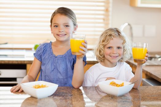 Siblings in the kitchen rising their glasses of orange juice