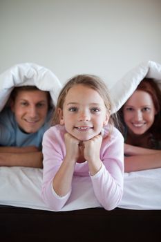 Smiling girl under bed cover together with her parents