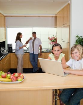 Siblings with their laptop in the kitchen with parents behind them