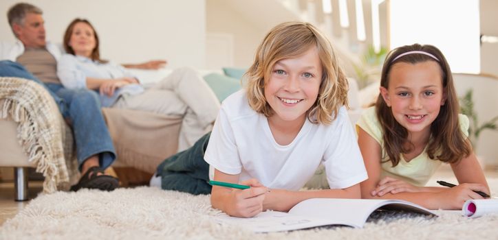 Siblings doing their homework on the floor with their parents behind them