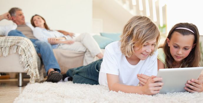 Siblings with tablet lying on the floor