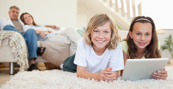 Siblings with tablet lying on the carpet