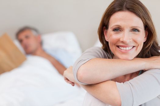 Smiling woman on the bed with reading husband in the background