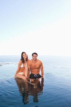 Couple sitting on the pool edge with sea in the background