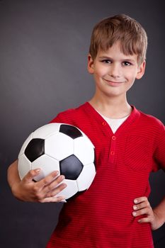 Cute boy is holding a football ball made of genuine leather isolated on a black background. Soccer ball