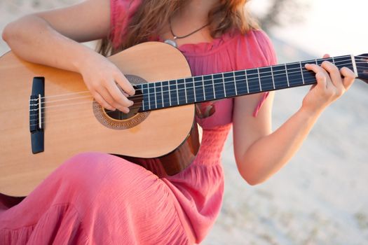 A girl in a dress playing a guitar shot on the nature