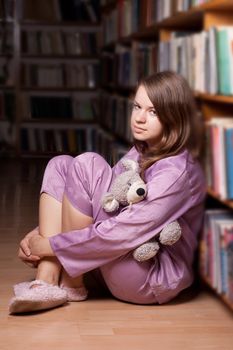 The girl in pink pajamas in the library among the books